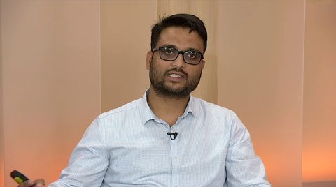 A man wearing glasses and a light blue shirt is presenting during an AWS Media Services webinar, seated in front of a neutral background.