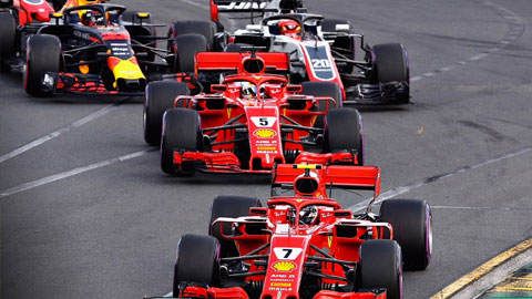 Close-up of Formula 1 cars racing on a track, with two red Ferrari cars leading the pack.