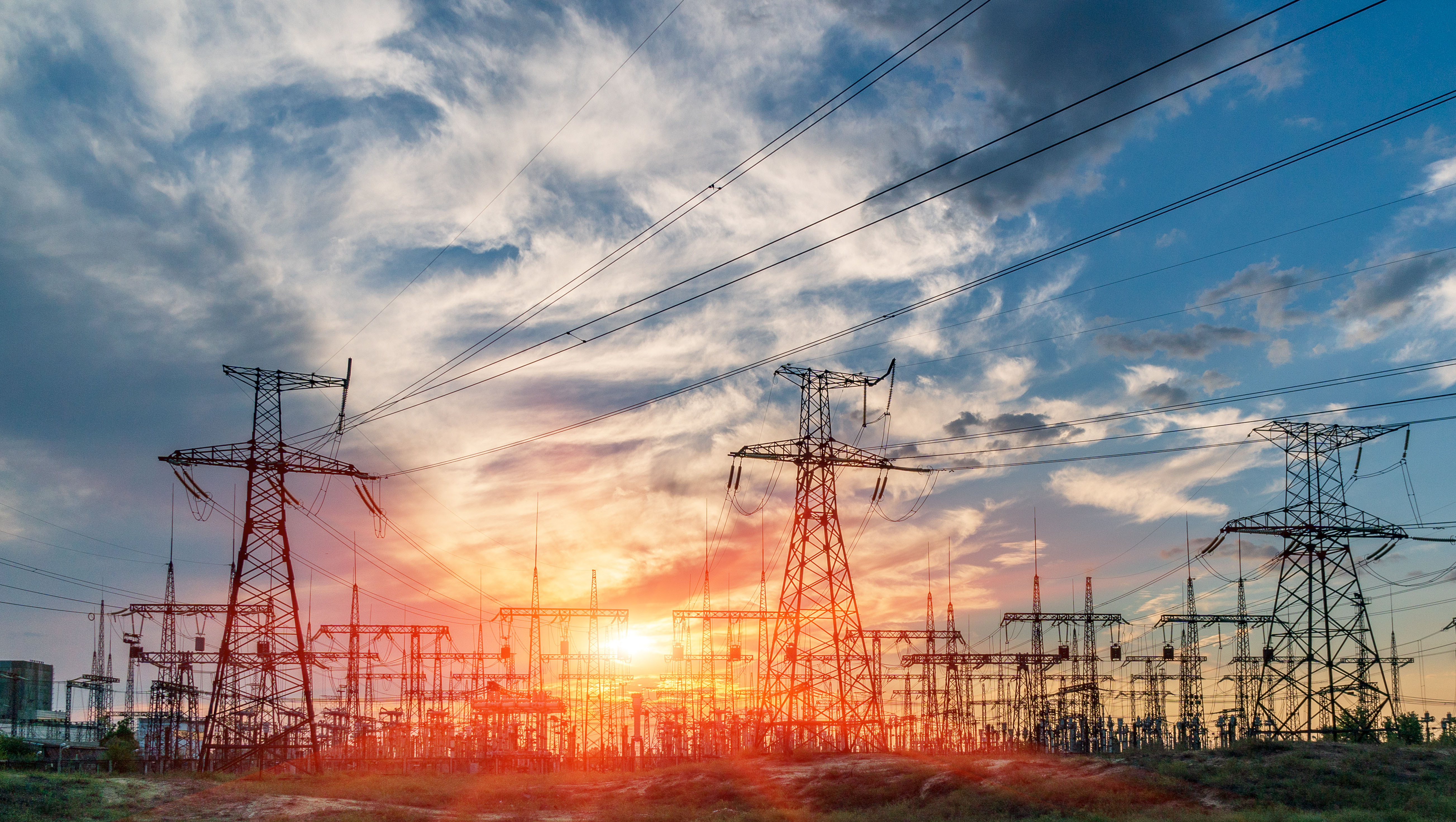 High voltage power transmission lines and towers against a dramatic sunset sky, representing infrastructure and energy distribution.