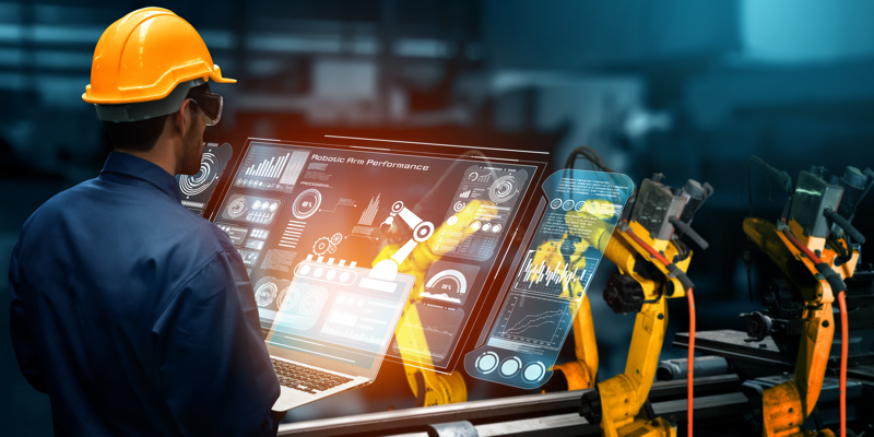 An engineer wearing a hard hat uses augmented reality technology to monitor and control robotic arms in a smart factory environment, illustrating advanced robotics and industrial automation.