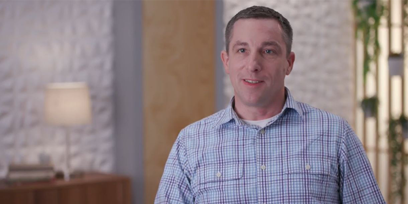 A male engineer from Amazon Lab126 is being interviewed in an indoor office setting, wearing a checked shirt and smiling at the camera.