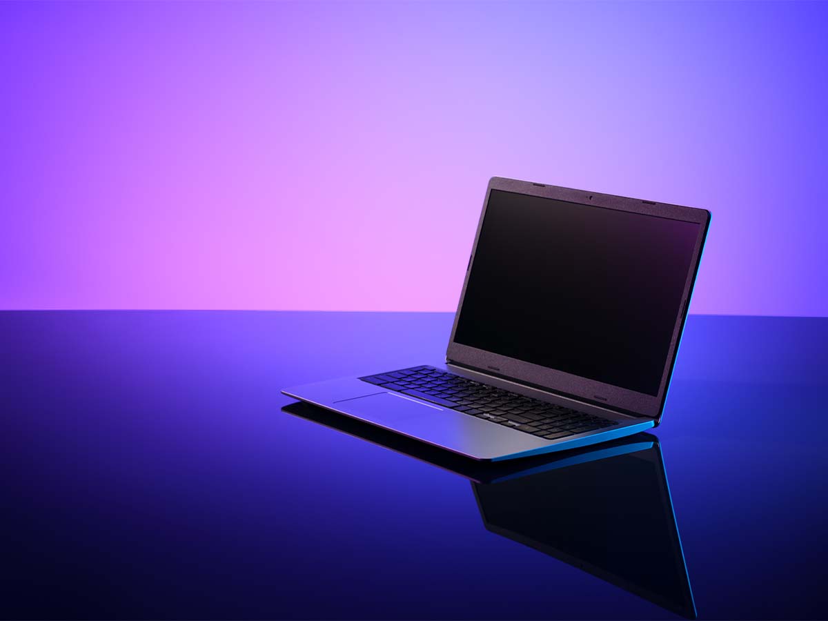A laptop computer is displayed on a reflective surface with a vibrant purple and blue gradient background.