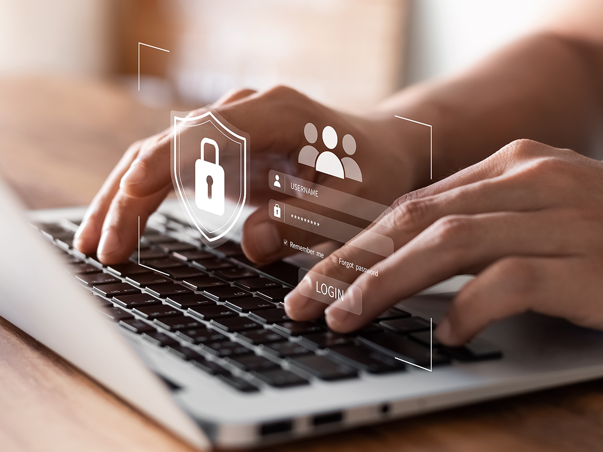 Close-up of hands typing on a laptop keyboard with digital graphics overlay showing a login screen and a security shield icon, representing secure user authentication and data protection.
