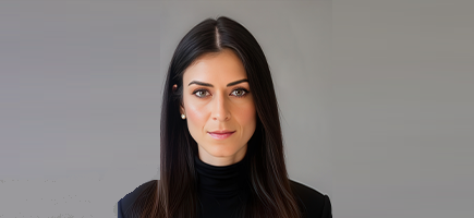 A person with long, straight brown hair wearing a black turtleneck against a neutral background.