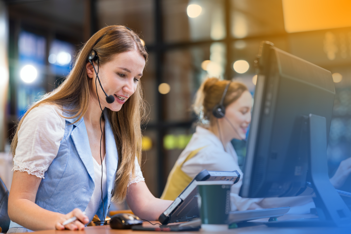 A call center operator wearing a headset works at a computer, representing cloud workloads and secure contact center operations.