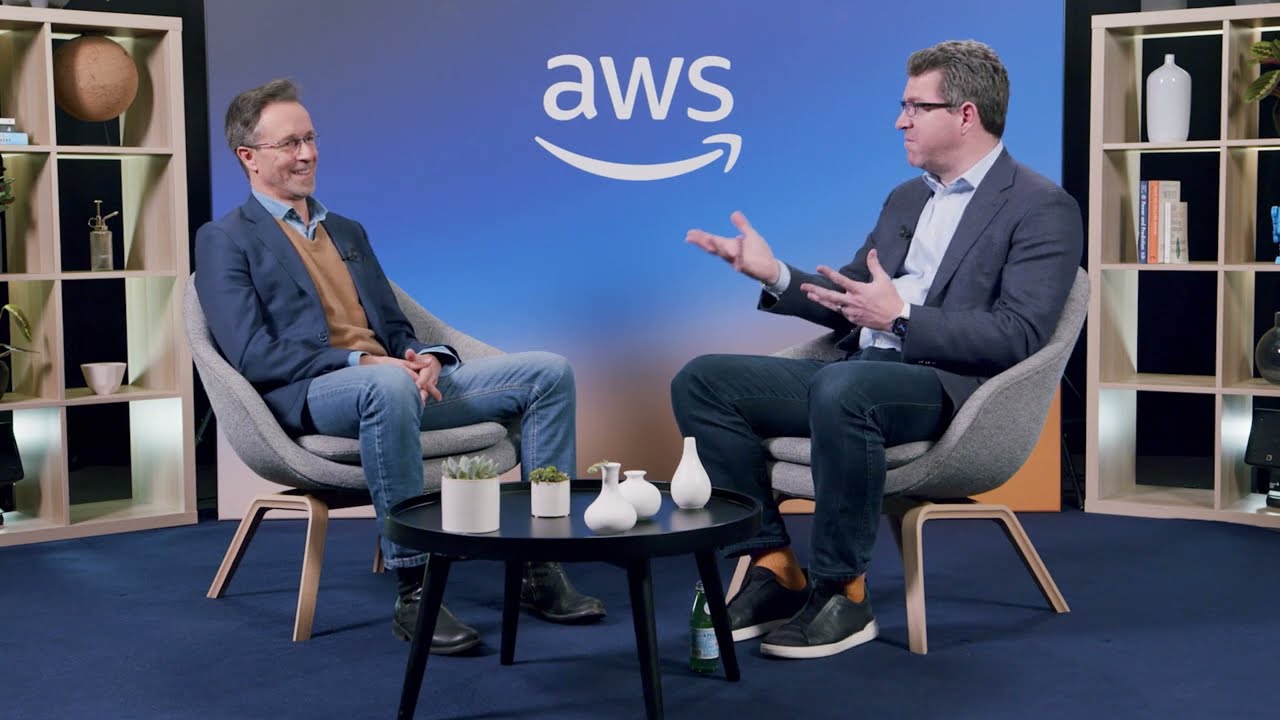 AWS interview set featuring two men engaged in conversation, seated in modern chairs with the AWS logo in the background.