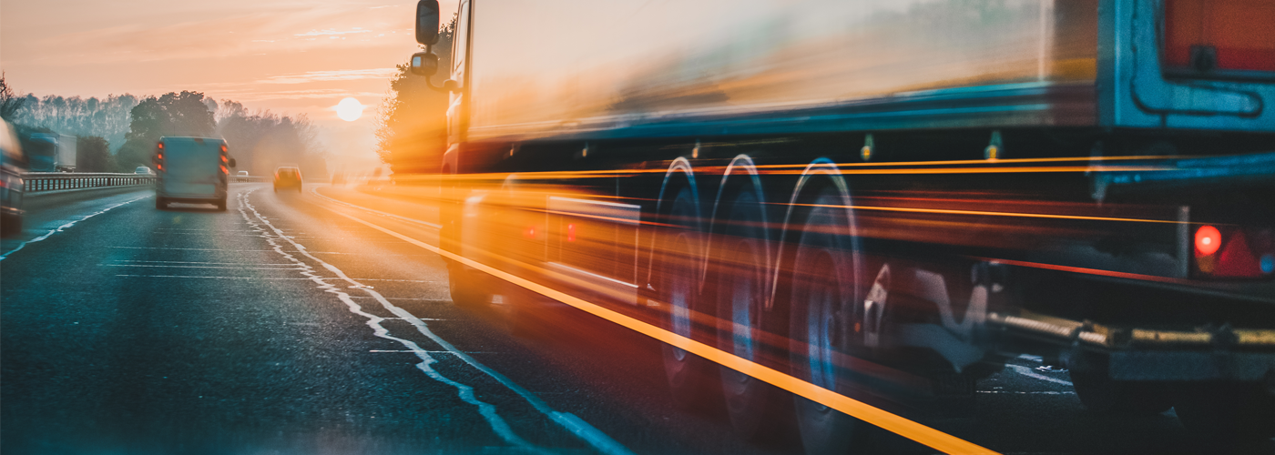 A truck driving on a highway at sunset, captured with motion blur to illustrate speed and movement in transportation and supply chain logistics.