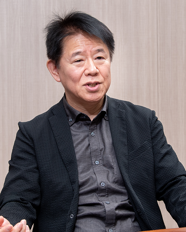 A man wearing a black jacket and dark shirt, seated in an interview or discussion setting with a neutral background.