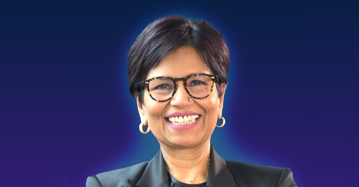 A person with short dark hair wearing a black blazer and hoop earrings, set against a gradient blue background.