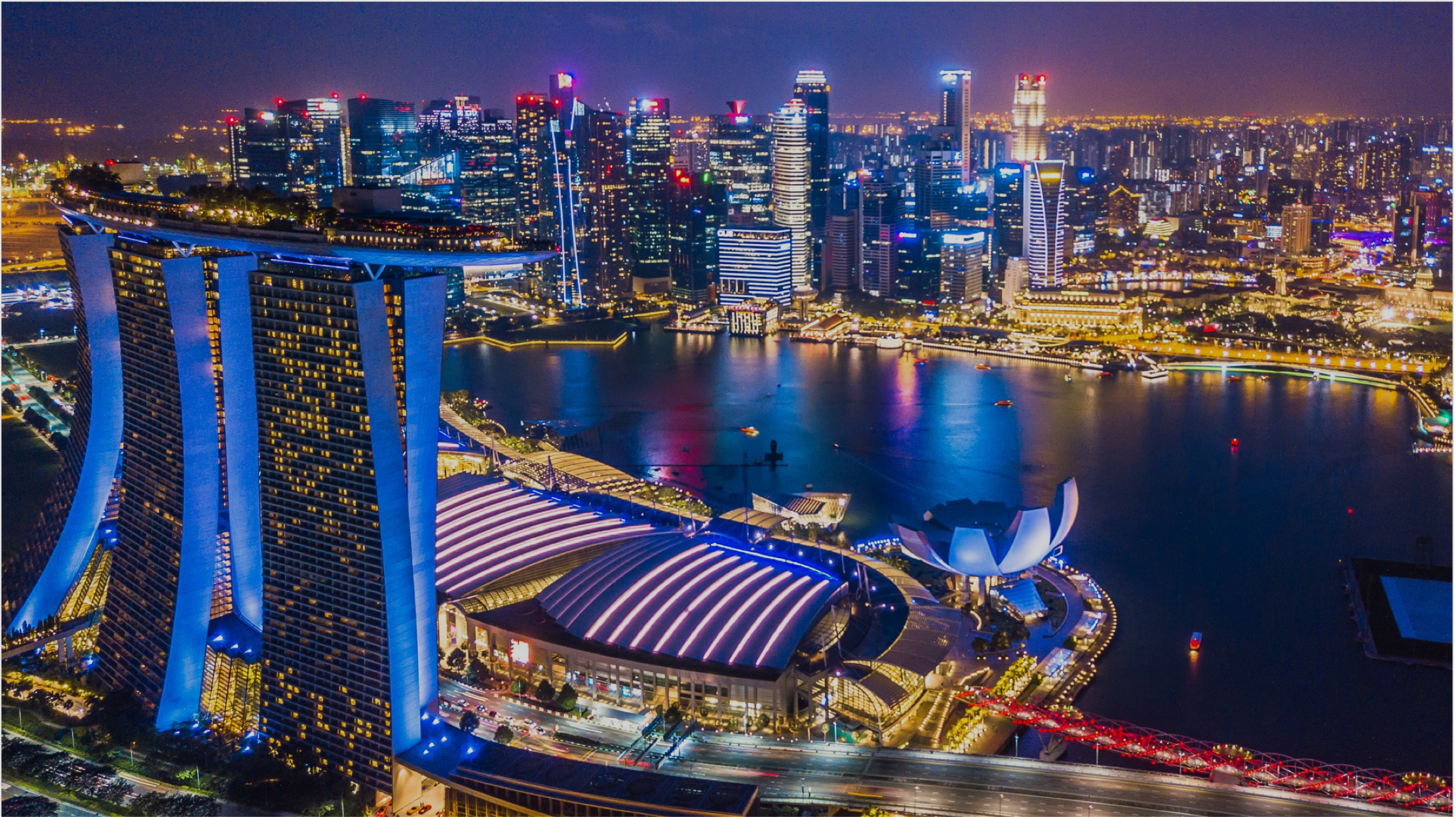 Aerial view of Singapore's Marina Bay Sands and surrounding cityscape illuminated at night, with vibrant lights reflecting on the water.