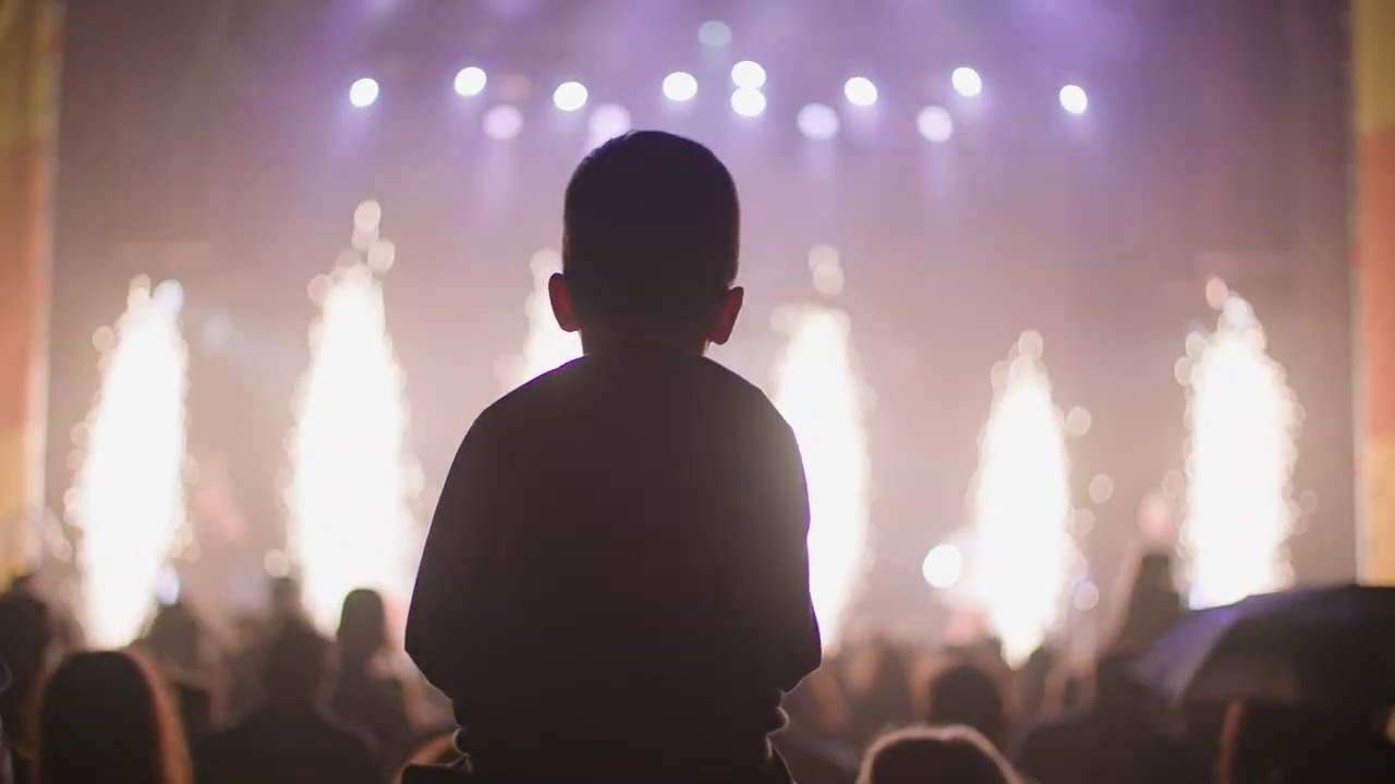 A silhouette of a child watching fireworks at a concert, with bright lights and pyrotechnics in the background, used as a YouTube thumbnail.