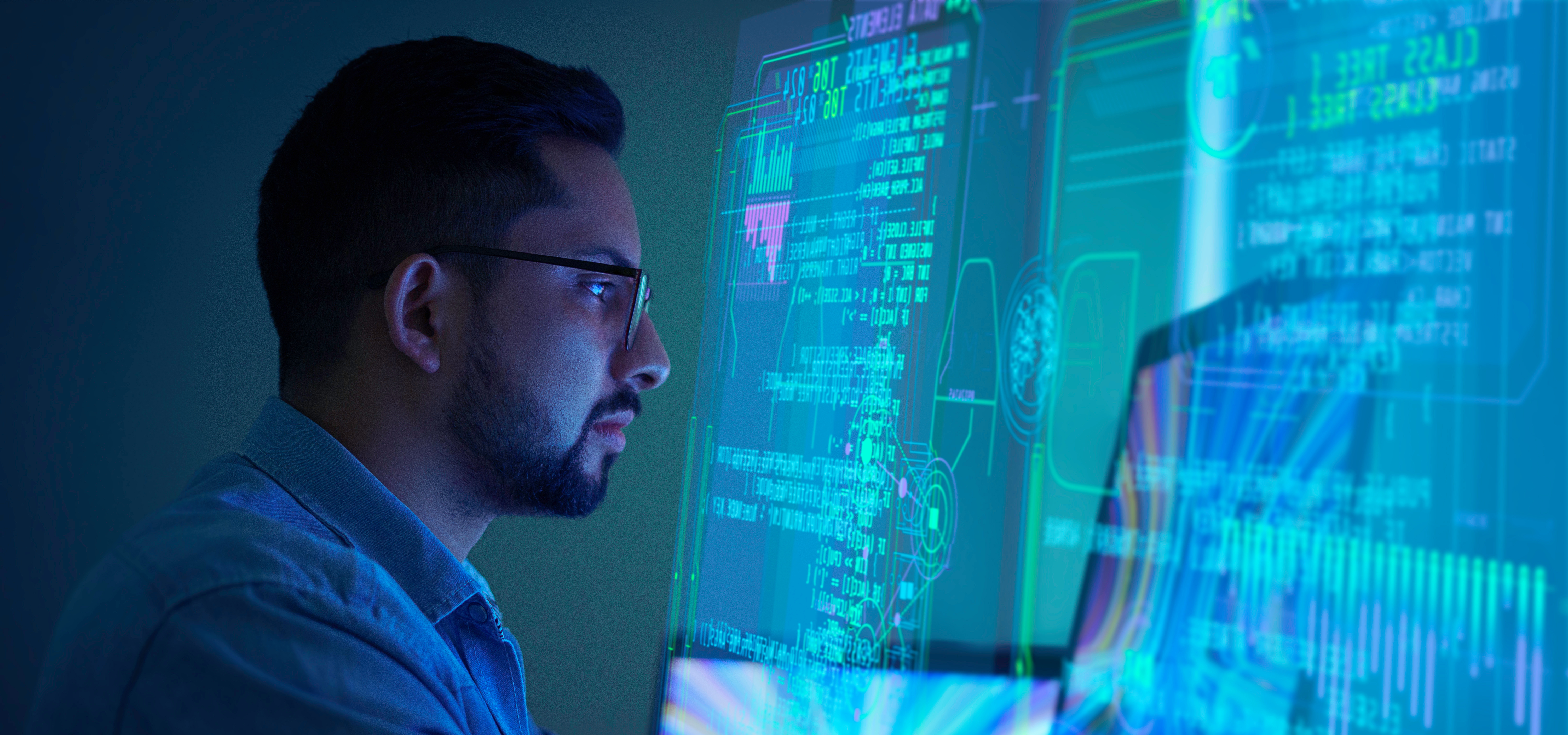 A person in a dimly lit room looking at a screen displaying colorful, glowing data and code.