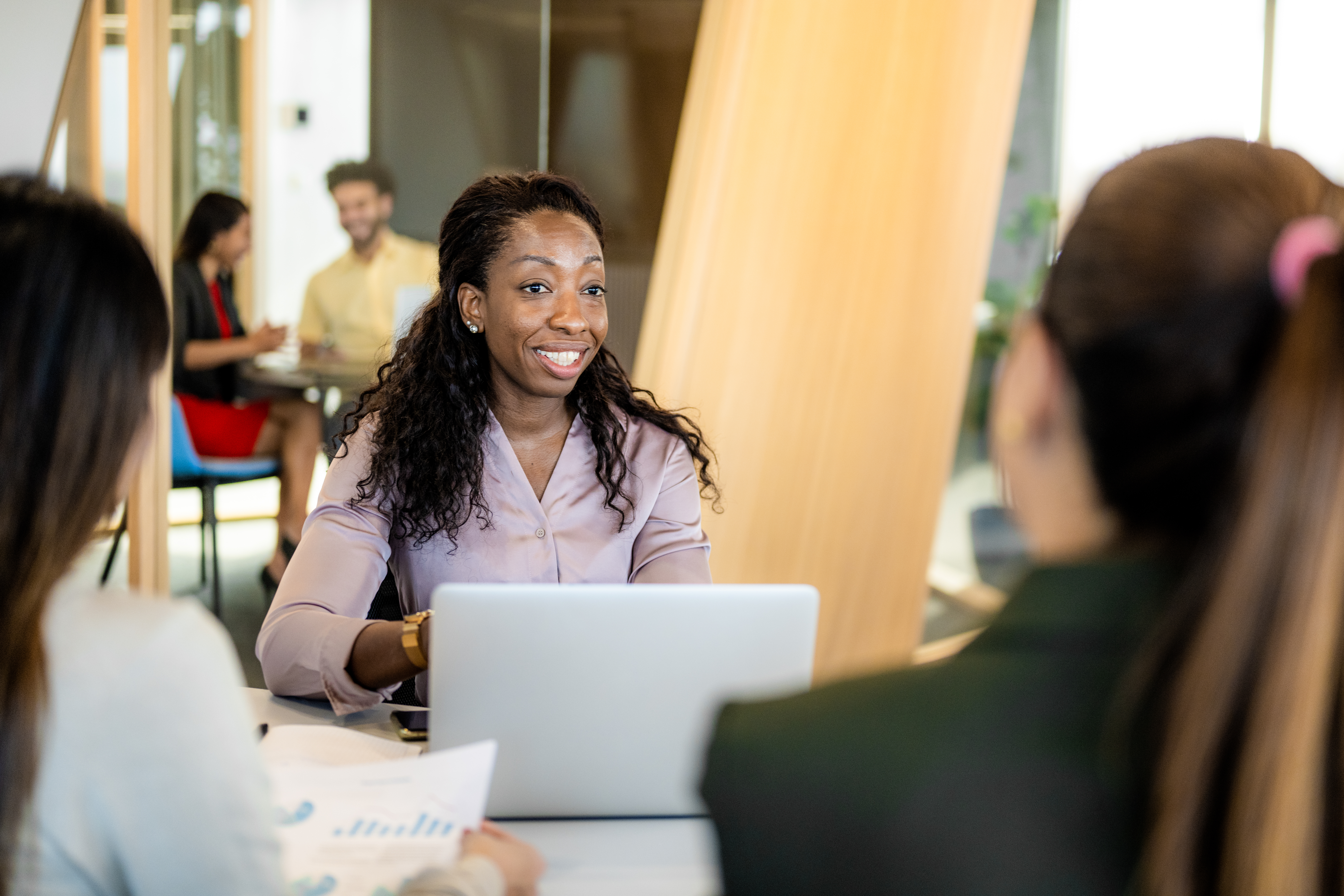 Group of businesswomen at a meeting in an open plan office talking while using computers.
