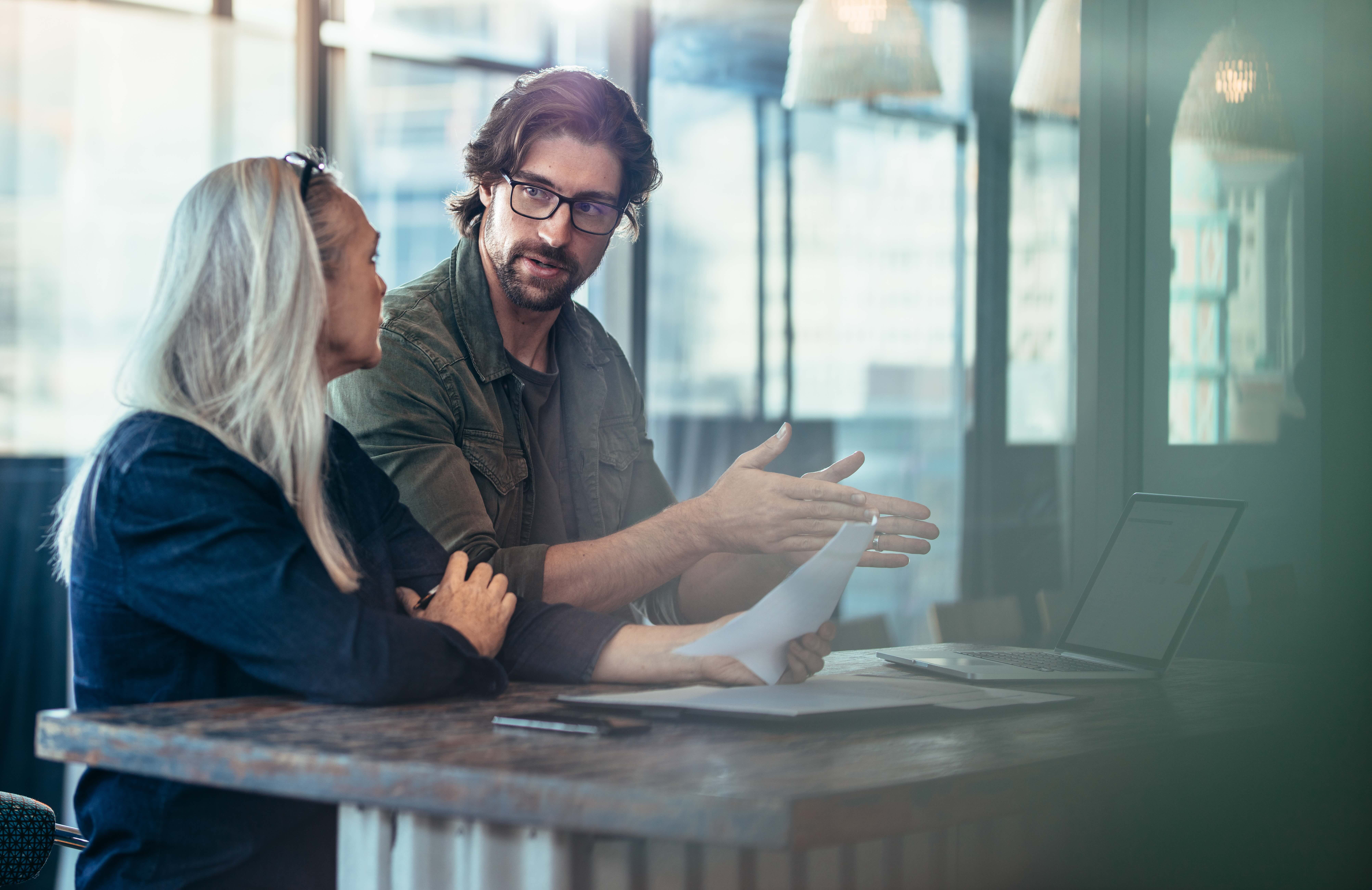Young man explaining his idea of business to mature female colleague at work. Business people having a meeting for project discussion.