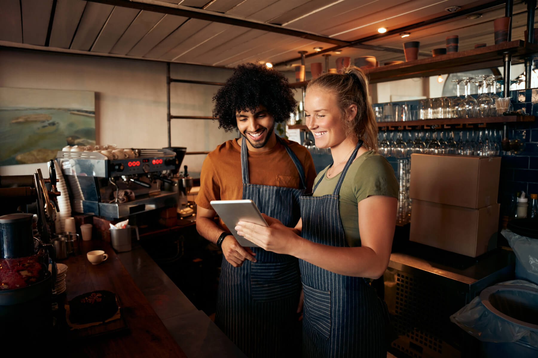 Hospitality staff smiling while looking at a tablet in a coffee shop