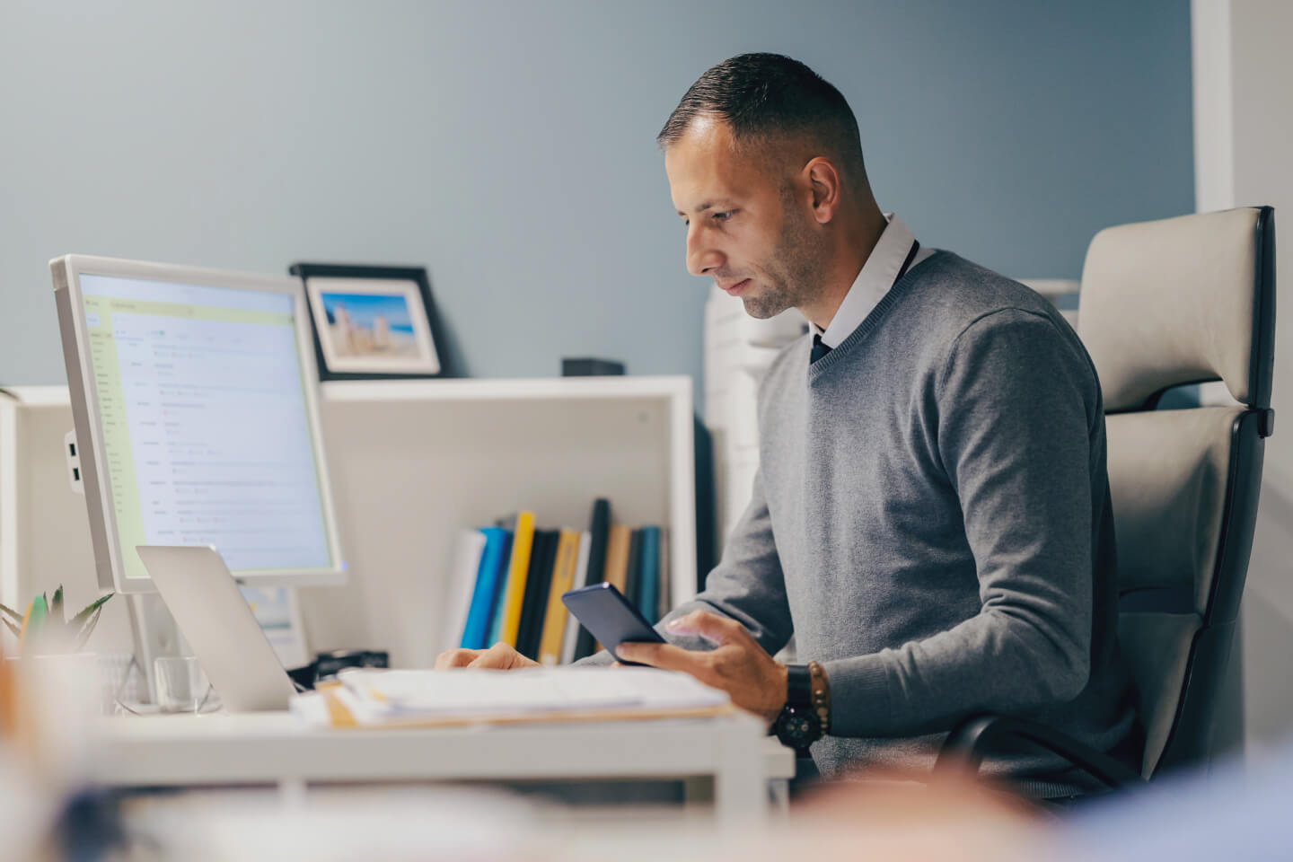 Smart business decision maker at desk holding phone and reviewing computer