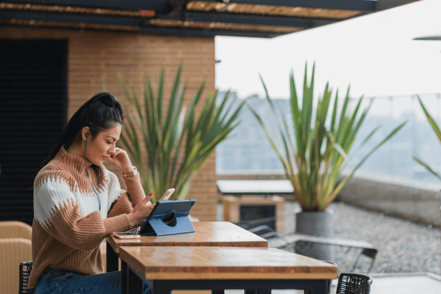 Technical content manager sat holding phone at remote outdoor workspace with a tablet on the table