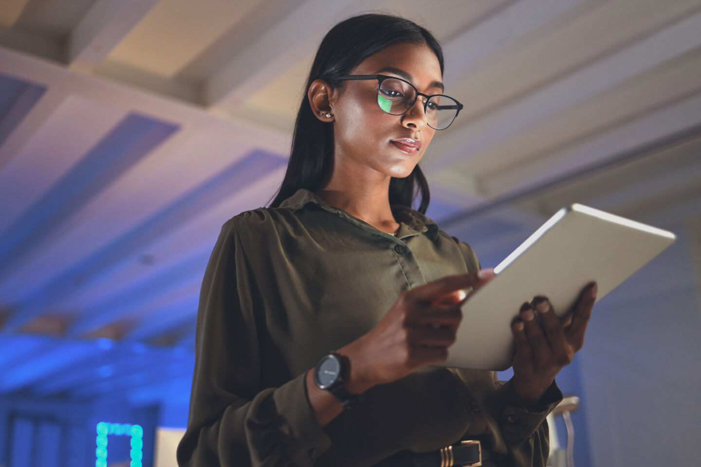 Technical decision maker stood in office holding a tablet with the screen reflecting off glasses