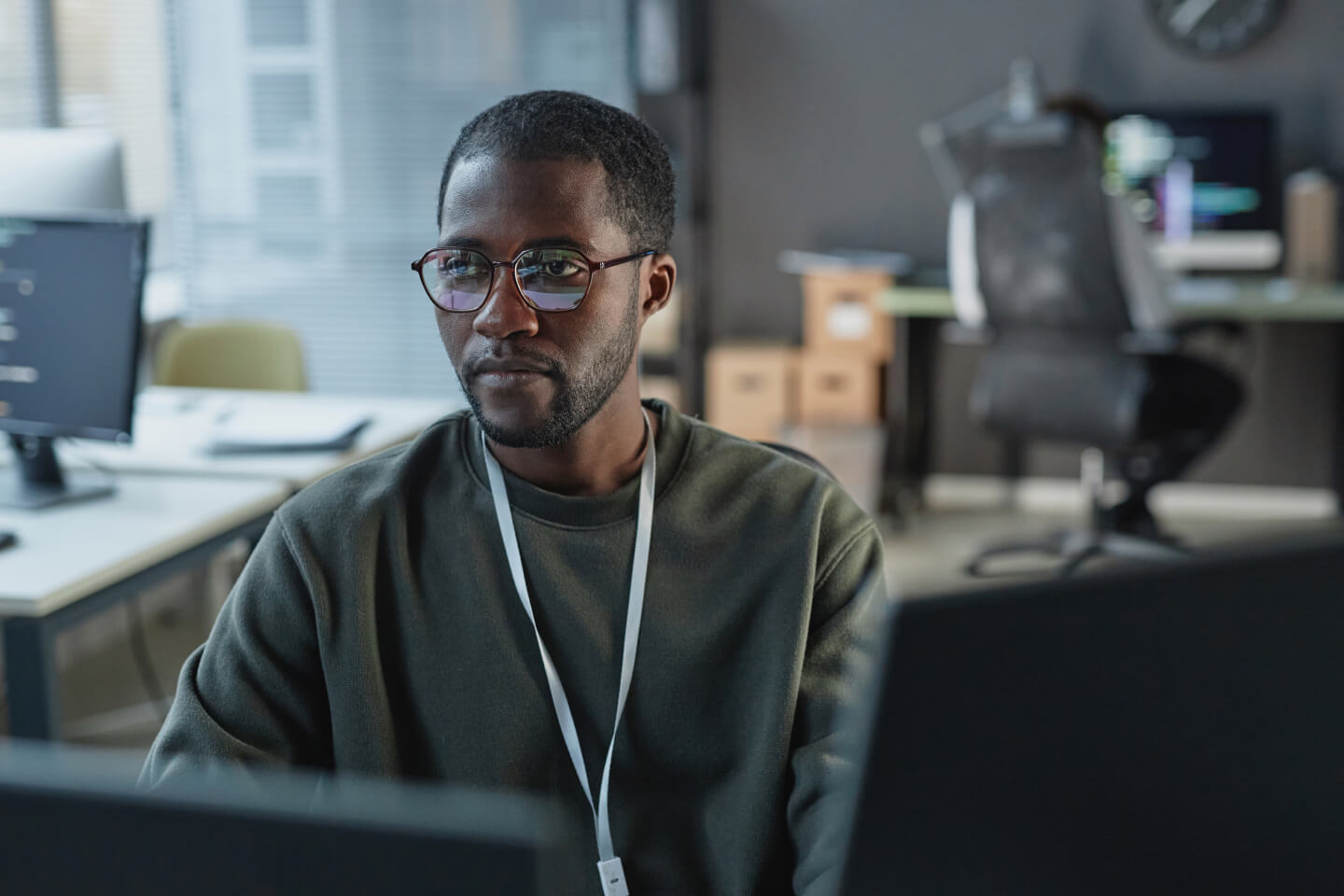 Technical decision maker wearing lanyard and working on dual screens in office
