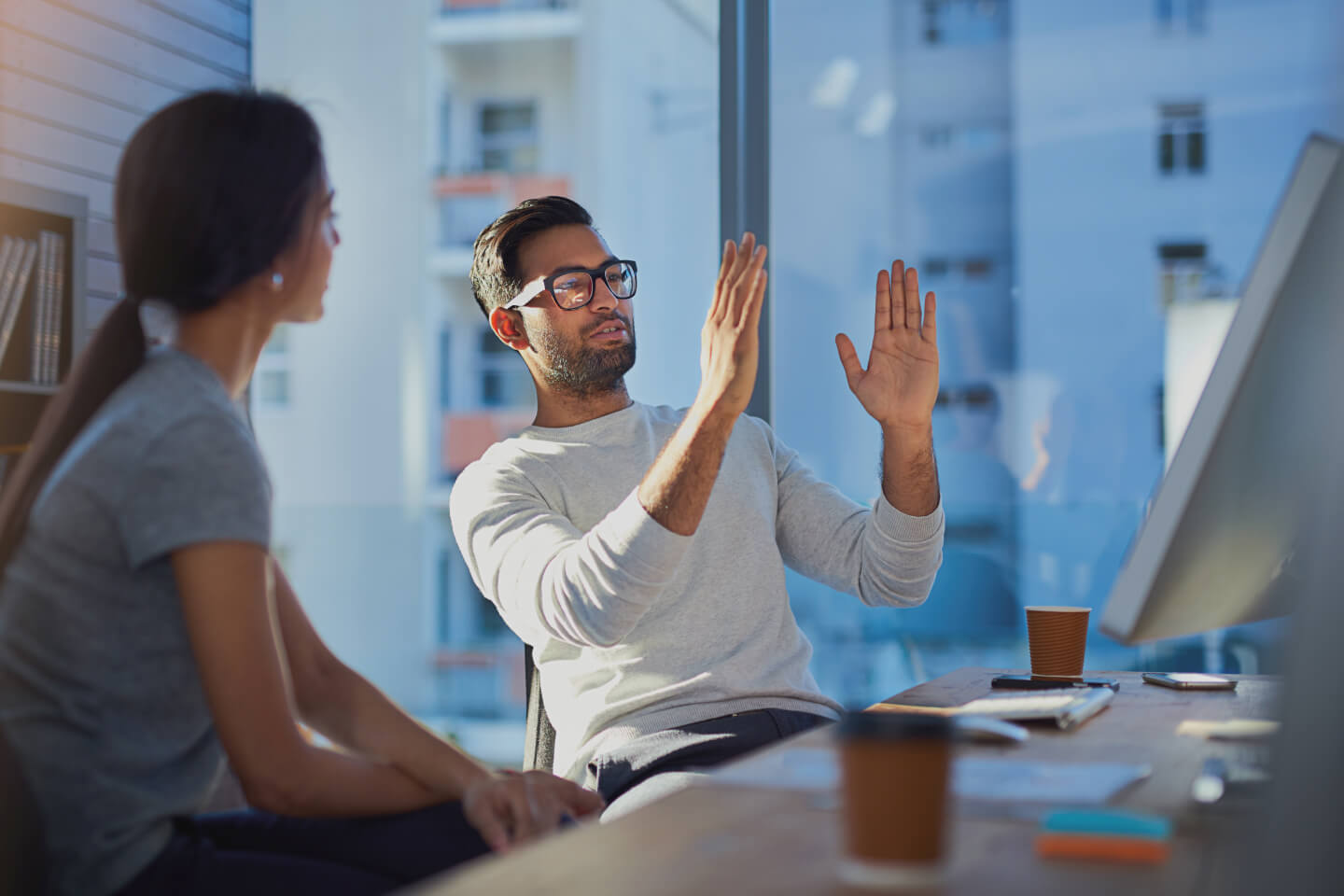 Technical expert gesturing scale with their hands sat with a colleague in front of large office windows