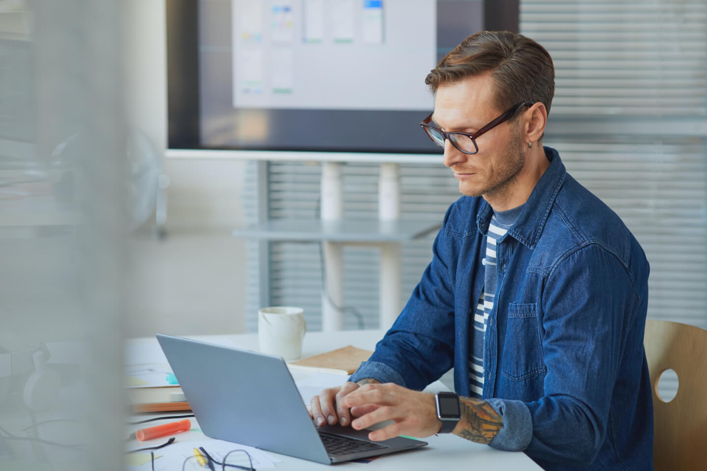 Technical expert working on laptop with web application wireframe designs on screen in the background