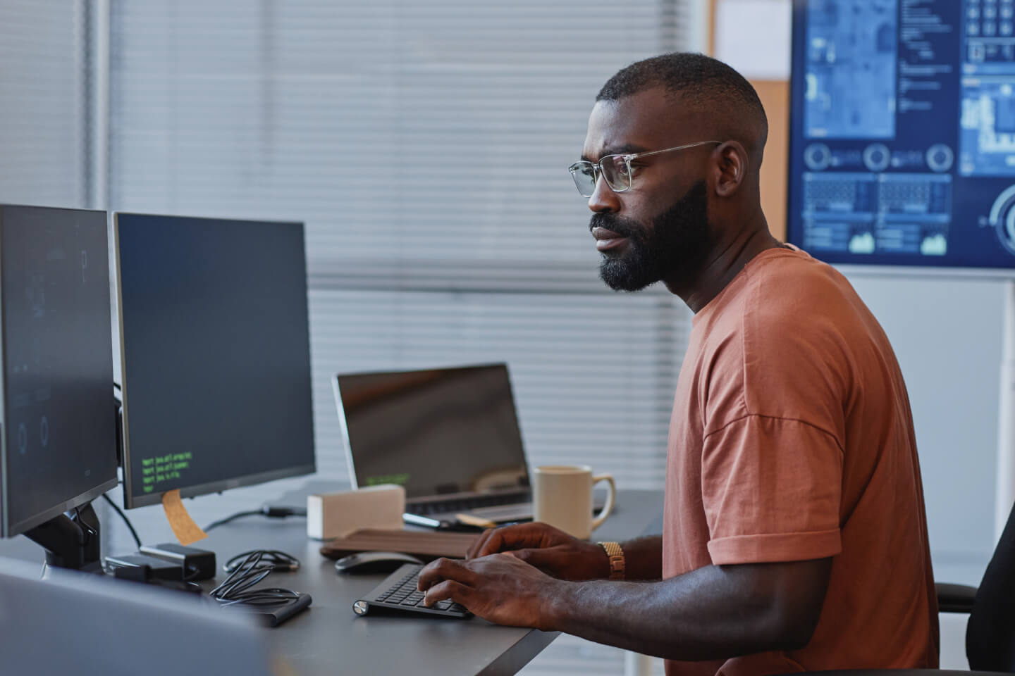 Technical expert working on multi-screen computer set up with data visualization on screen in the background