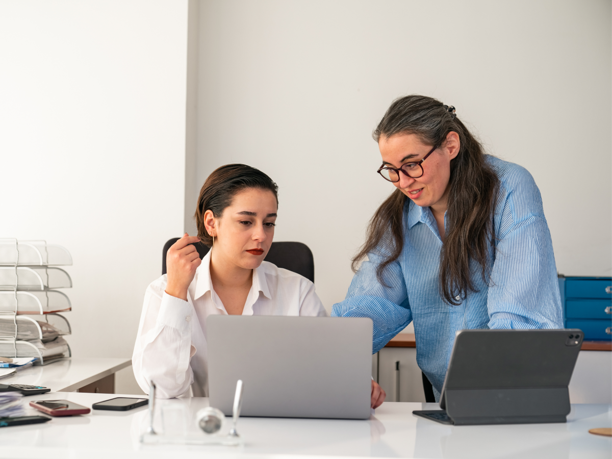 Two people working together at a desk with laptops and office supplies.