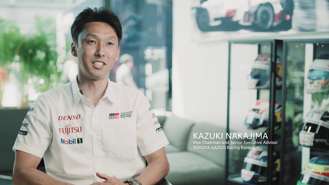 YouTube video thumbnail featuring an interview with Kazuki Nakajima, Vice Chairman and Senior Executive Advisor of TOYOTA GAZOO Racing Europe, seated in a motorsports environment with display cases of racing helmets and car images in the background.