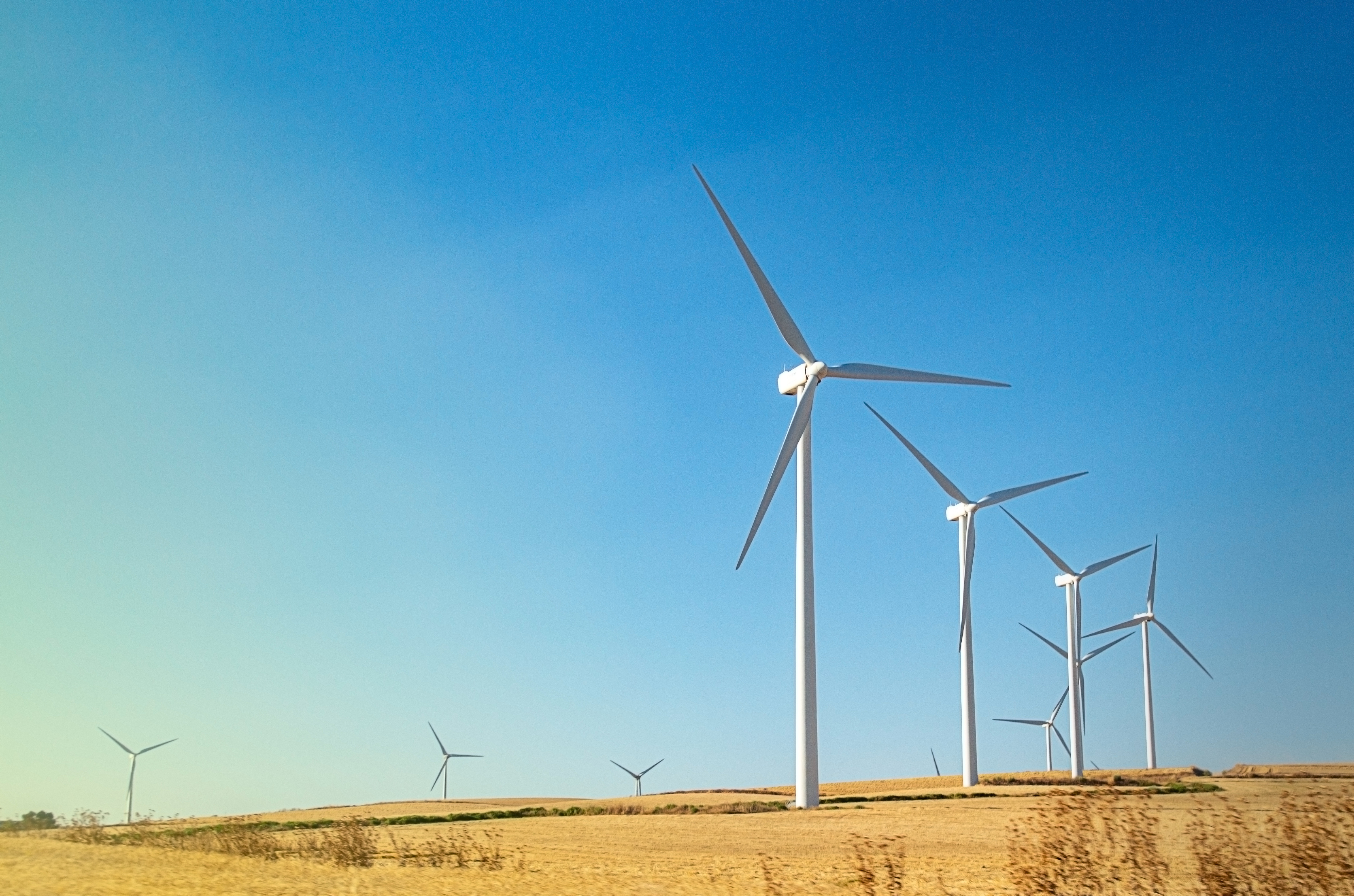 Windmills wind turbines farm power generators against landscape against blue sky in beautiful nature landscape for production of renewable green energy. Friendly industry to environment. Concept of sustainable development technology.