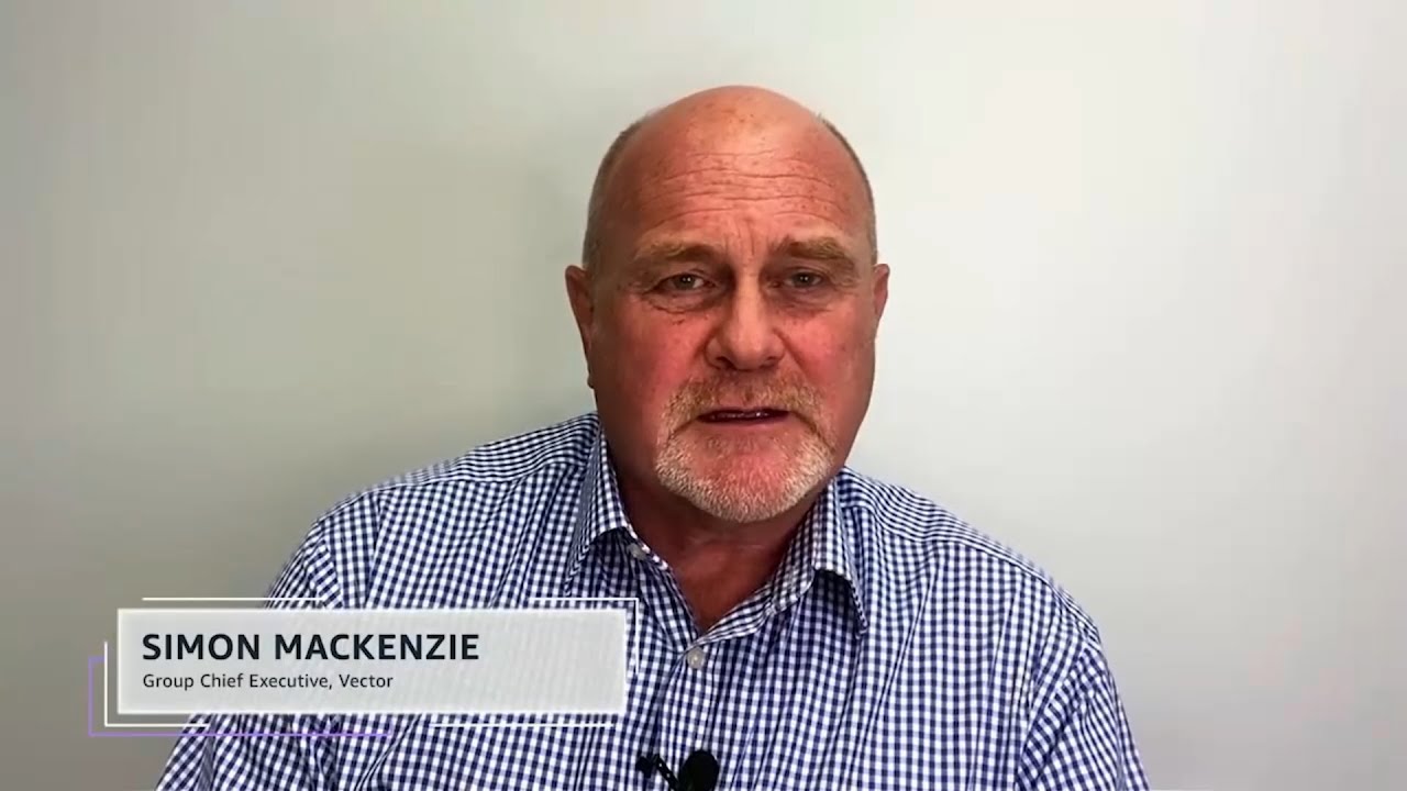 A man in a checkered shirt sits against a plain background, with an overlay reading 'Simon Mackenzie, Group Chief Executive, Vector.' This image appears to be from a video interview or testimonial related to a case study.