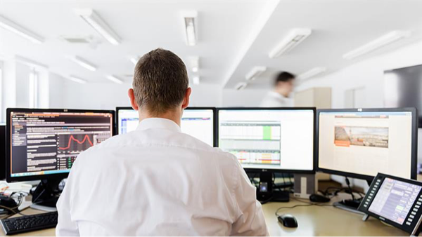 An office worker is seated at a desk using multiple computer monitors to analyze and review data in a modern office environment.