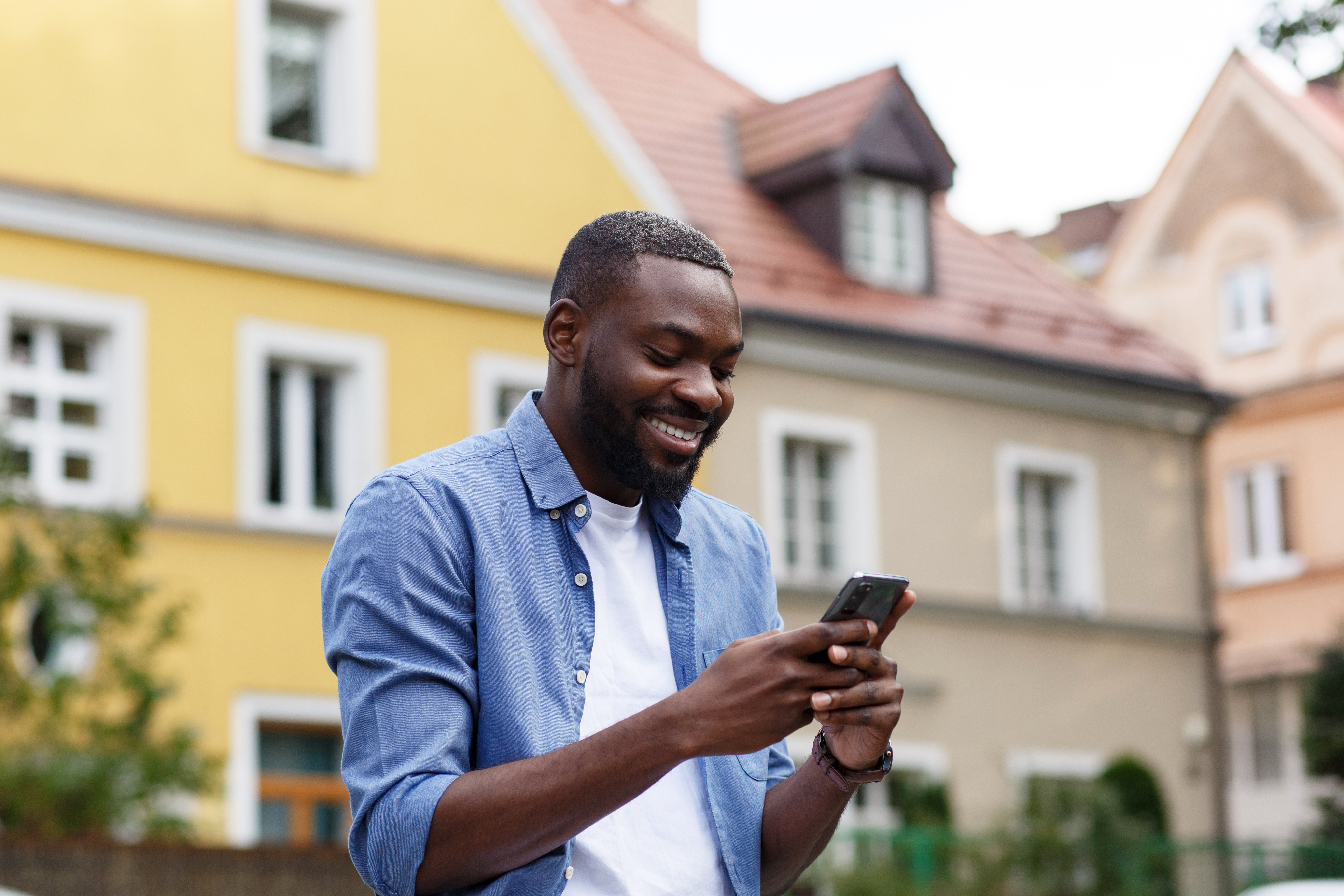 Handsome Afro-American man using smartphone and smiling. Happy man using mobile phone apps, texting message, browsing internet, looking at smartphone. Young people working with mobile devices.