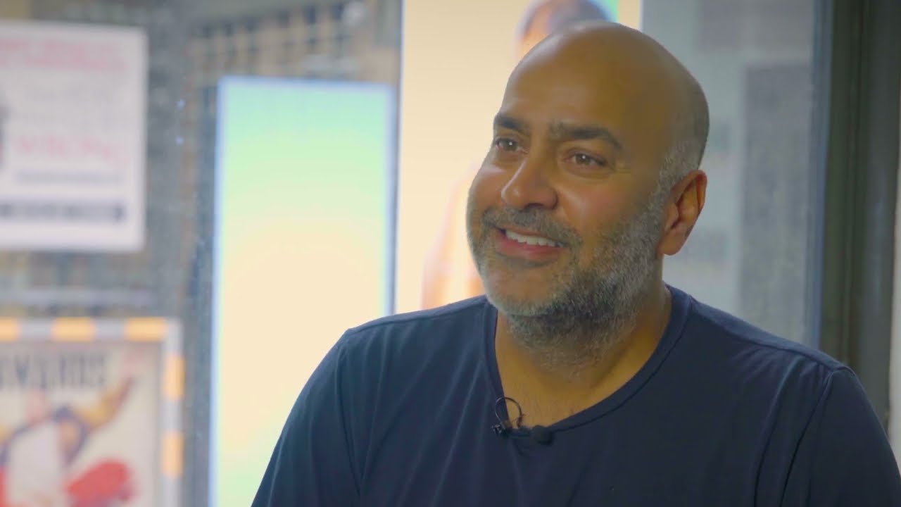A YouTube thumbnail image featuring a smiling man being interviewed in a well-lit, casual setting.
