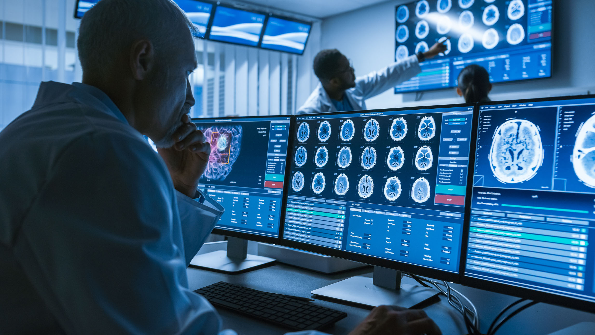 Doctors analyzing detailed brain scans displayed on multiple computer monitors in a modern healthcare technology environment.