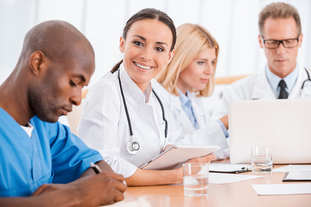 Doctor at the meeting. Beautiful young female doctor smiling while sitting together with her colleagues at the meeting