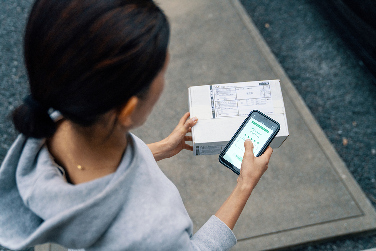 A person holding a package and using a smartphone to rate their delivery experience on a mobile app.
