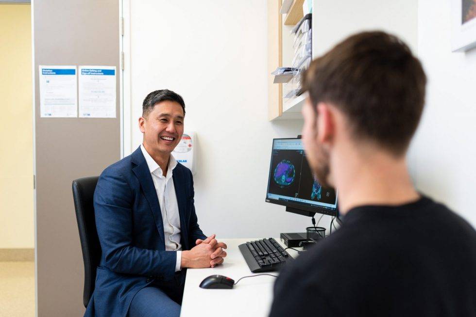A doctor consults with a patient in a modern clinic, utilizing digital tools and a computer displaying medical images, representing digital pathways in healthcare.