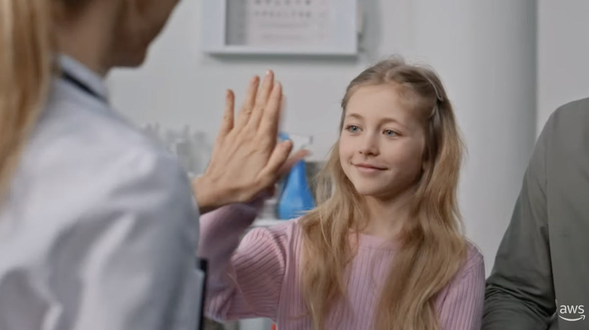 A doctor in a white coat giving a high-five to a child wearing a pink sweater in a medical setting.