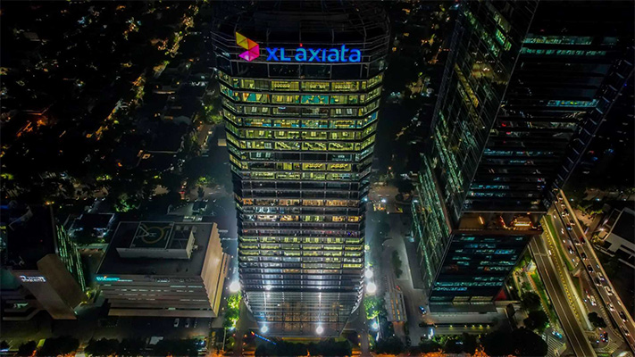 Aerial night view of the XL Axiata headquarters building illuminated in a cityscape, with the XL Axiata logo visible on the rooftop.