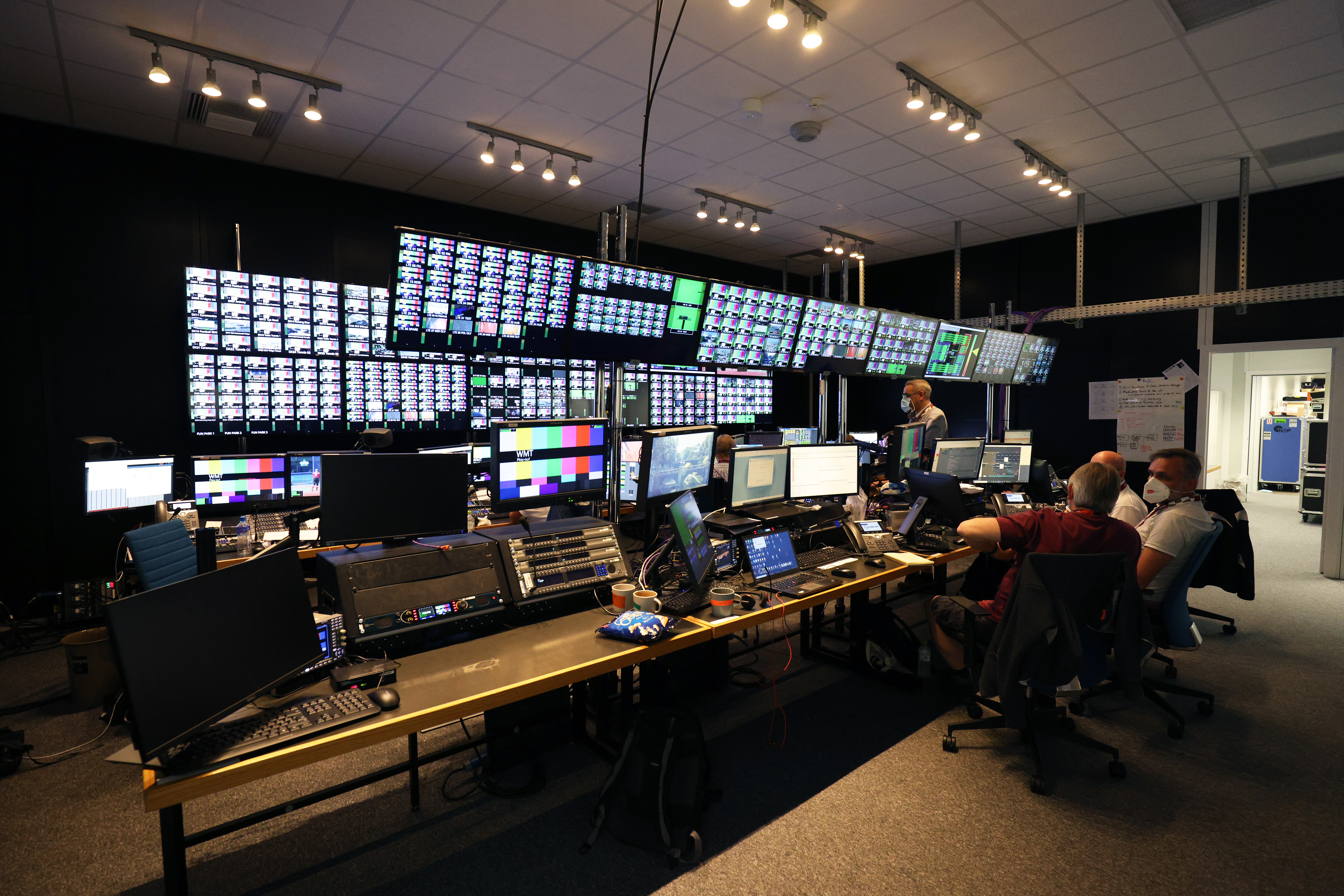 Broadcast control centre in Tokyo for IBC Eurosport 2021, featuring multiple operators working at rows of computer stations and large video walls displaying numerous broadcast feeds and monitoring screens.