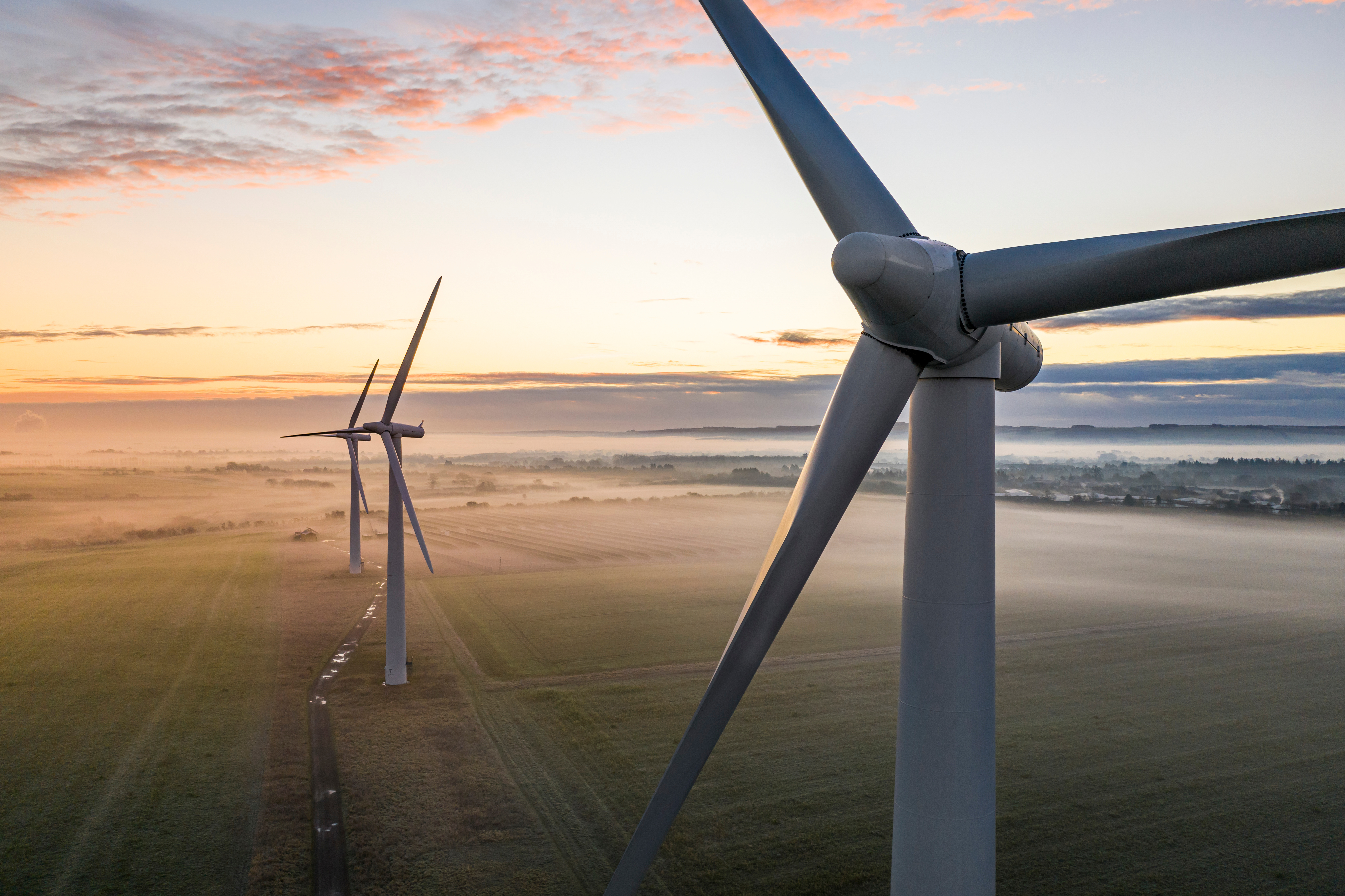 Aerial view of three wind turbines in the early morning fog at sunrise in the English countryside