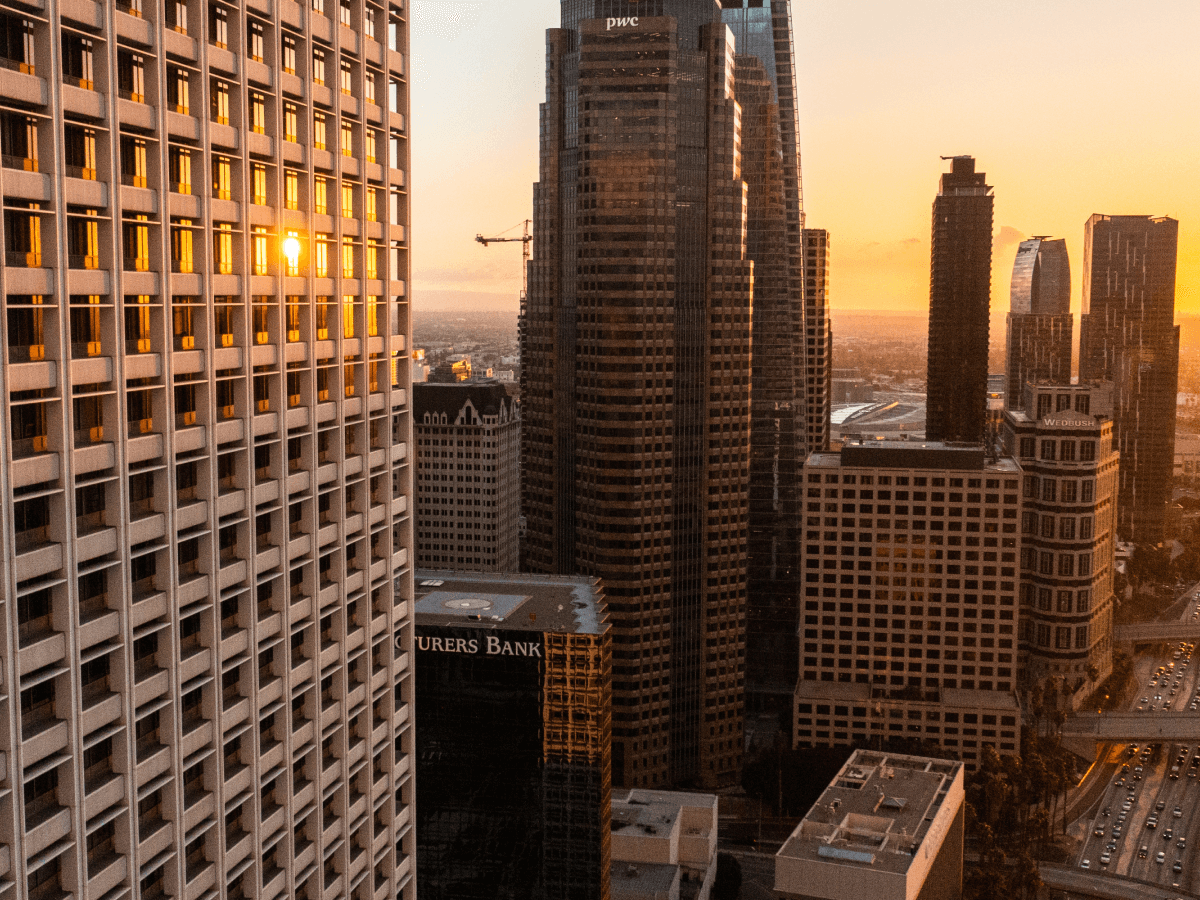 Sunset reflecting on the windows of tall buildings in a cityscape with a warm orange glow.