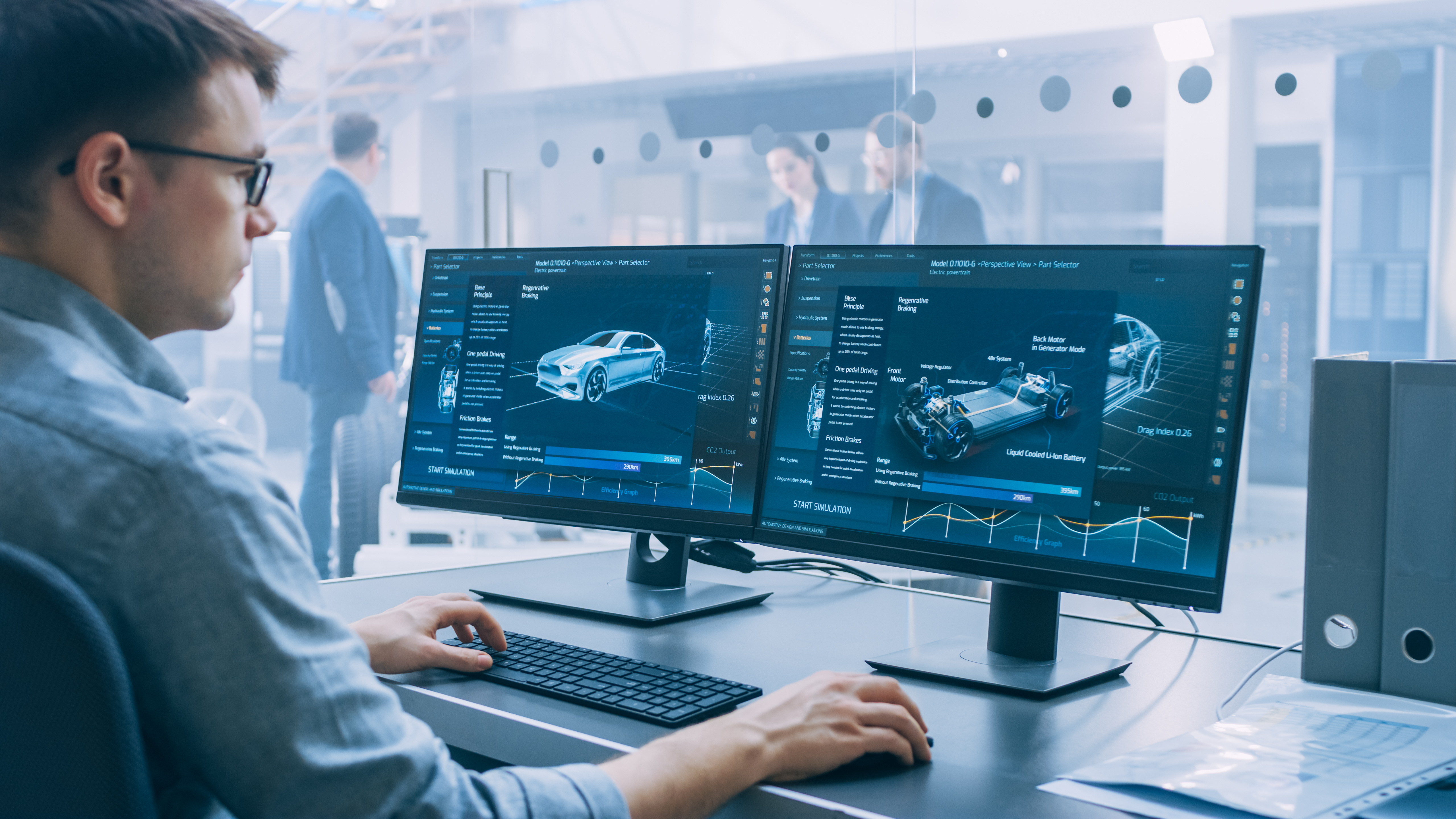 Professional Engineer Works on a Computer with a 3D CAD Software and Tests the Electric Car Chassis Prototype with Wheels, Batteries and Engine Standing in a High Tech Development Laboratory.