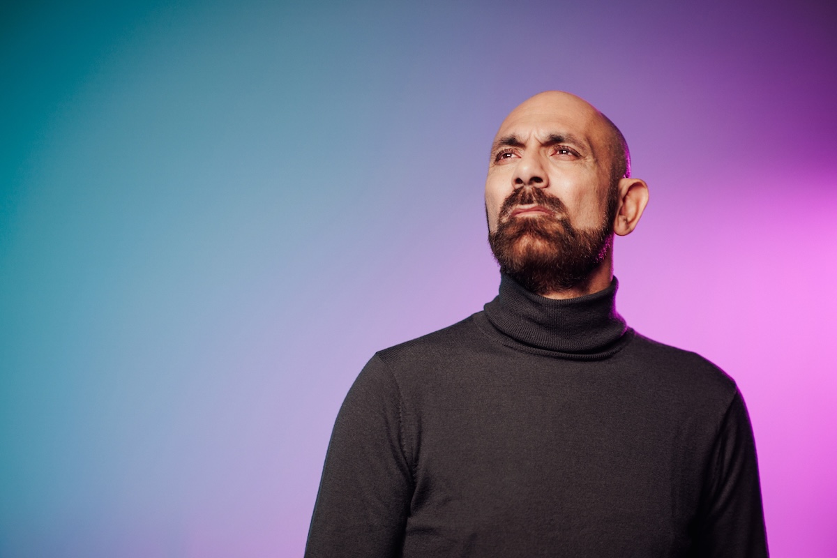 Person wearing a black turtleneck against a gradient background of blue and purple.