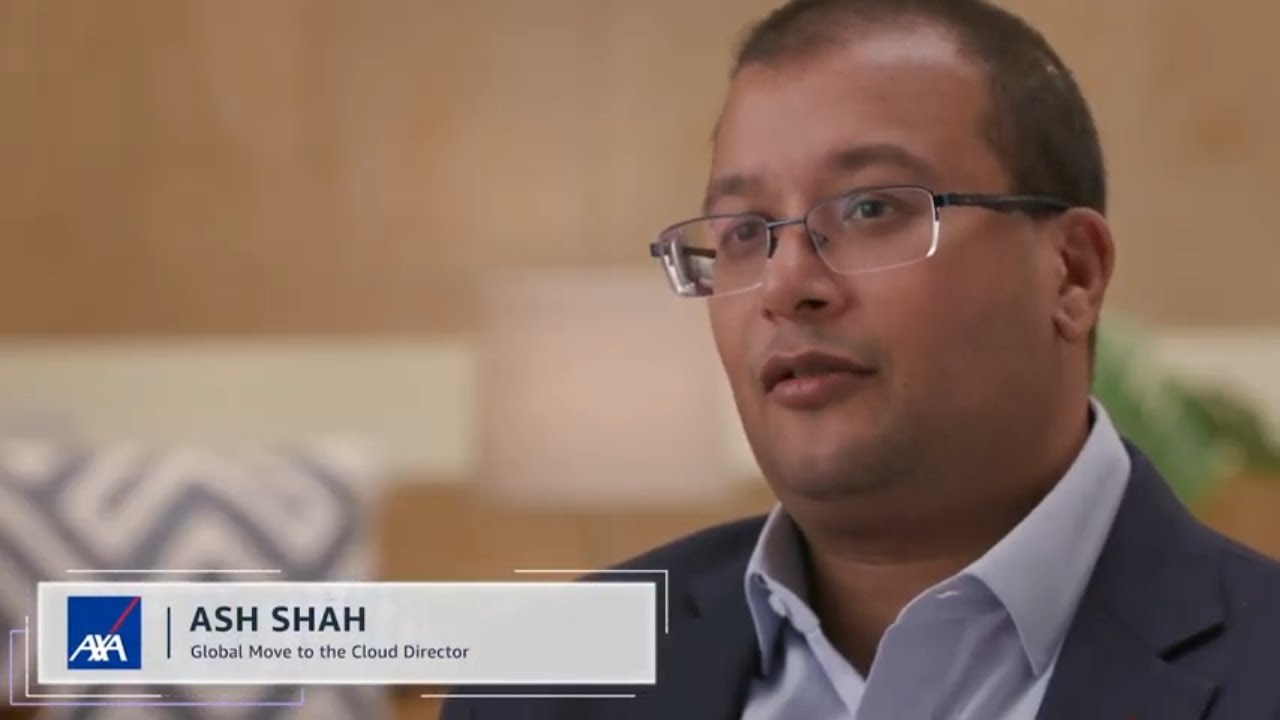 A person in business attire being interviewed indoors, with an AXA logo and title 'Global Move to the Cloud Director' displayed on-screen. This image is from a solution case study video.