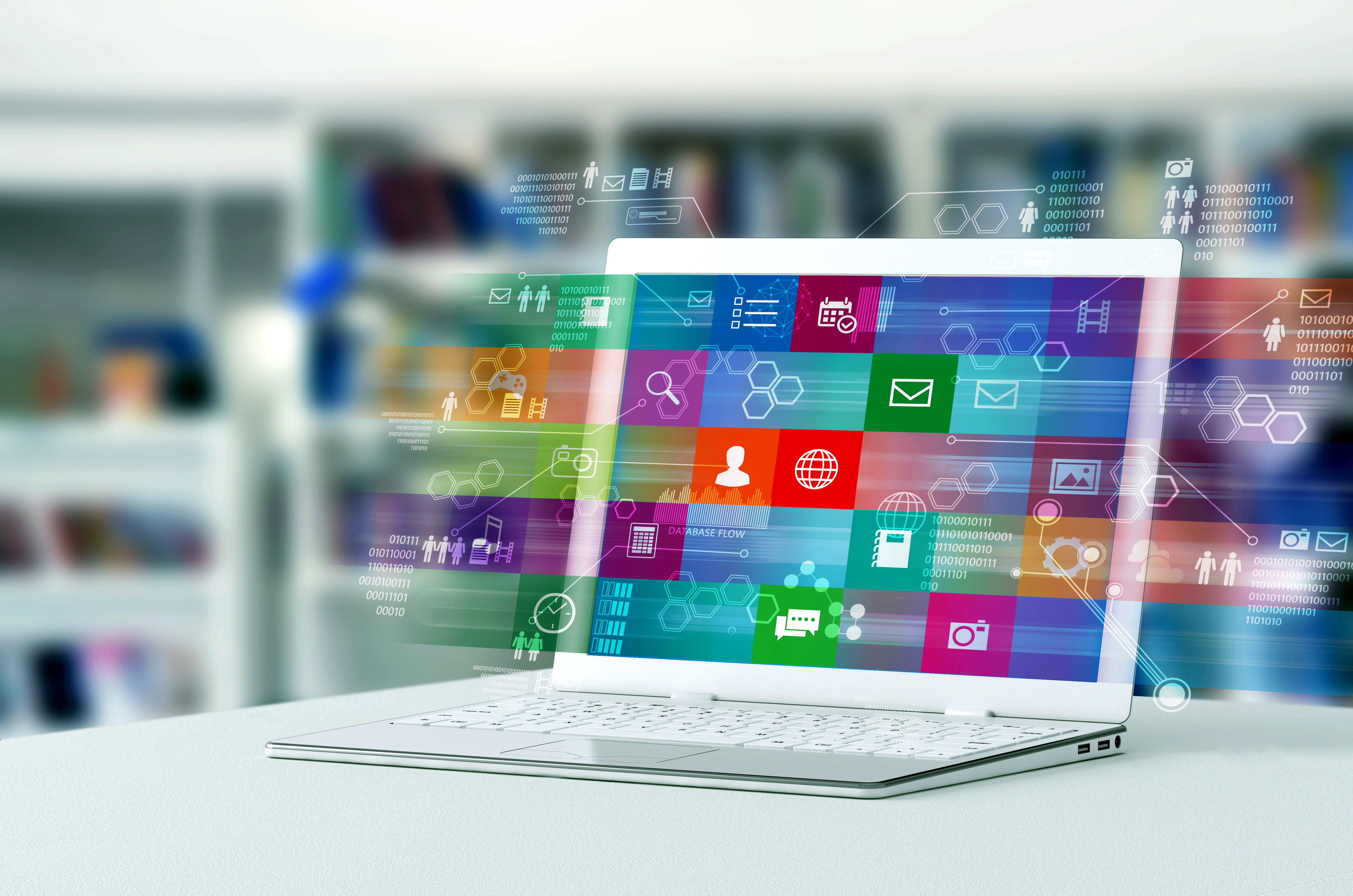 A laptop computer displaying a colorful digital interface with various multimedia and internet application icons, representing online connectivity and digital software solutions. The background is a blurred office or library setting.