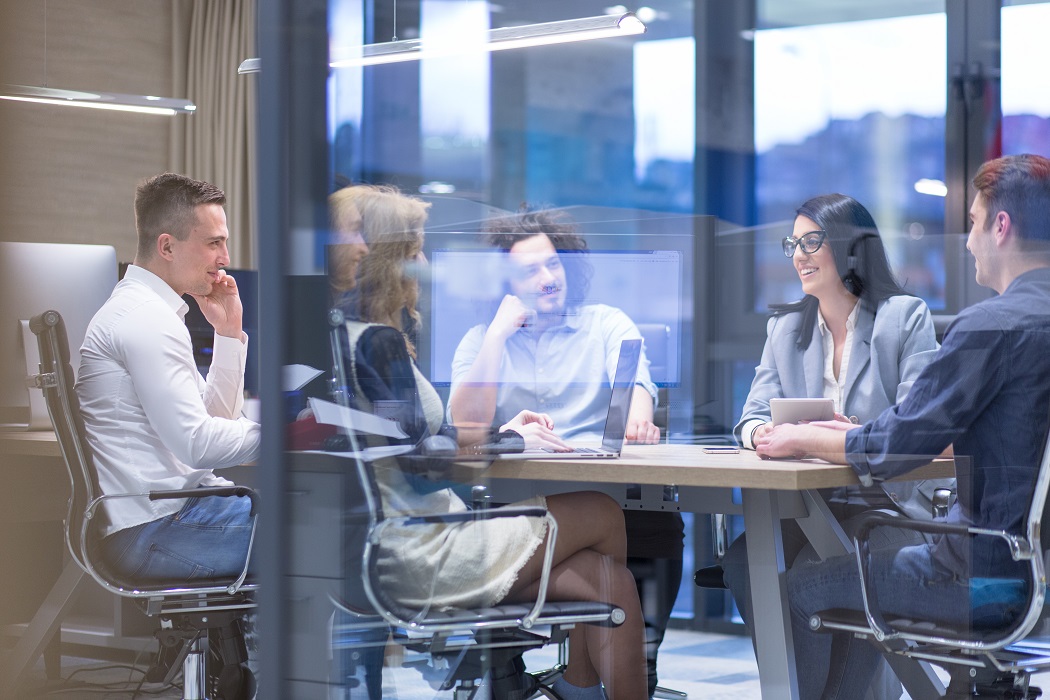 A group of professionals having a meeting around a conference table in a modern office with large windows.