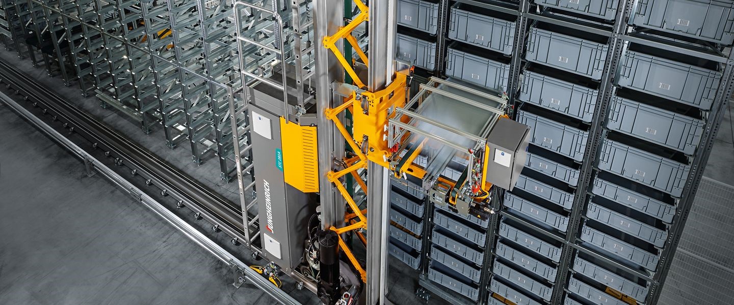A high-angle view of a Jungheinrich automated stacker crane operating in a modern warehouse storage system with metal shelves and plastic storage bins.