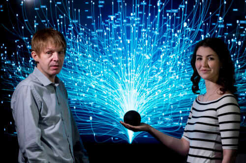 Two people standing with a black sphere in their hands in front of a glowing blue digital network background, symbolizing technology and connectivity.