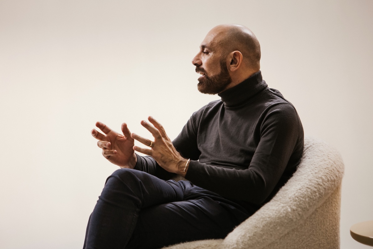 A person wearing a black turtleneck and seated in a textured armchair, gesturing with their hands.